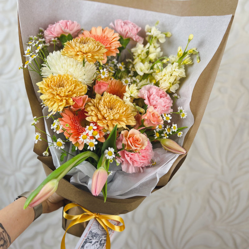 A hand-tied bouquet featuring warm pastel flowers with a the Sun tarot card