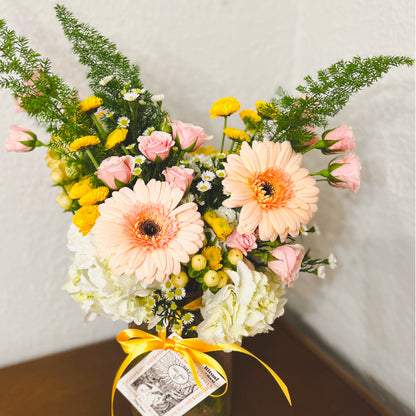 Peach-colored daisies and other pink, yellow and white flowers in a vase