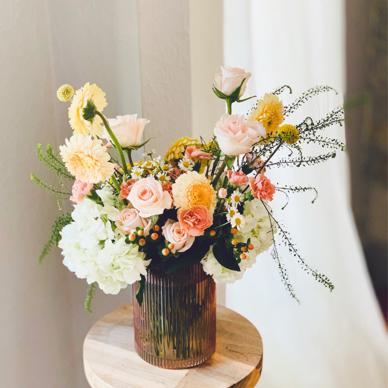 An assortment of warm pastel blooms in a pretty pink vase