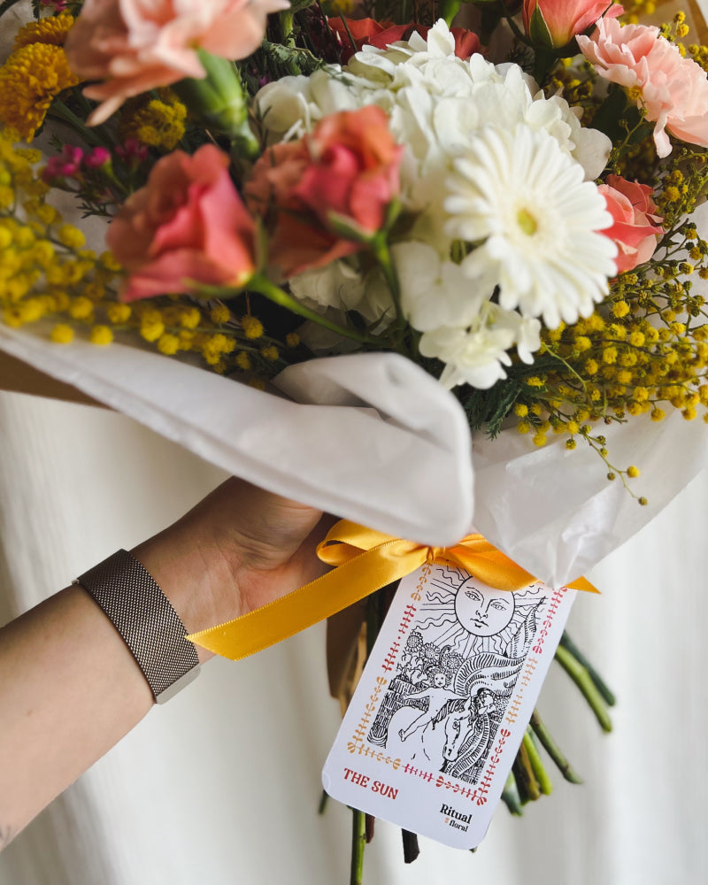Close up view of a The Sun tarot card tied to a bouquet of flowers