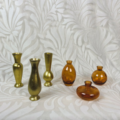 Two sets of 3 bud vases. One set is all gold while the other is amber glass.