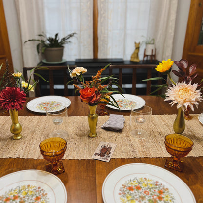 A dinner table set for Thanksgiving with a trio of gold bud vases and the three of cups tarot card