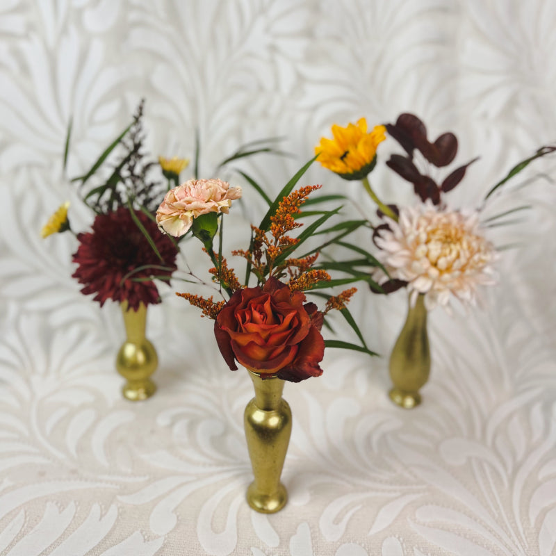 Three gold bud vases filled with autumn flowers on a white background