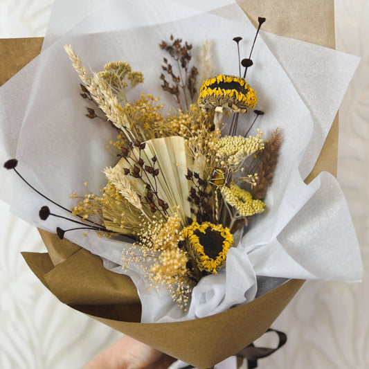 A yellow, tan, and brown dried flower bouquet wrapped in paper