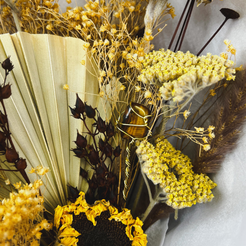 An up close shot of a tiger's eye crystal in a bouquet of yellow and tan dried flowers