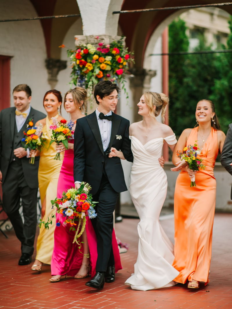 Bride and groom walk along an outdoor patio with their wedding part surrounding them.