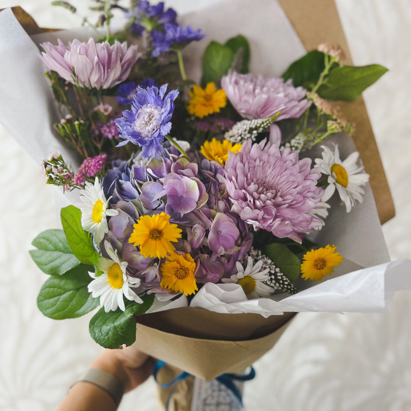 Standard size designer's choice bouquet featuring purple and yellow flowers with greenery