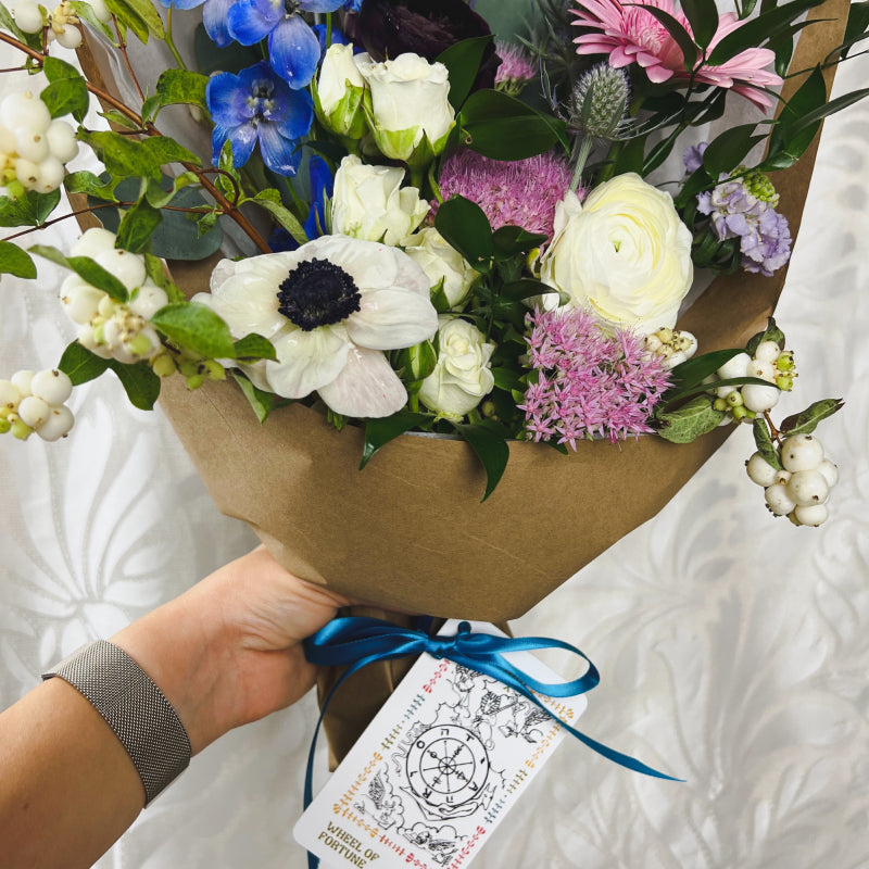 Wrapped flower bouquet with a Wheel of Fortune tarot card tied to it with ribbon